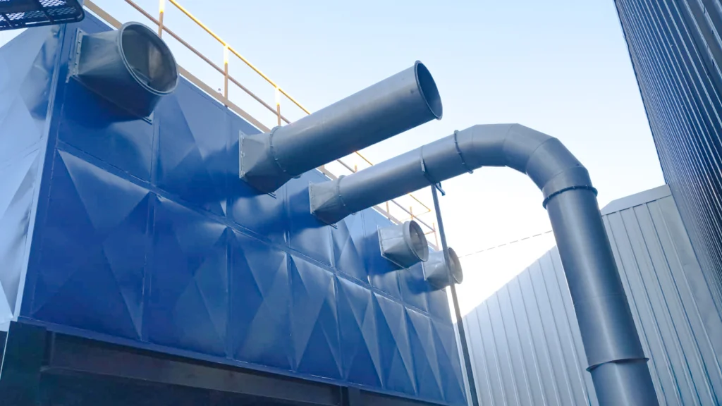 Colector de polvo tipo baghouse con ductería y toberas de conexión en fachada azul