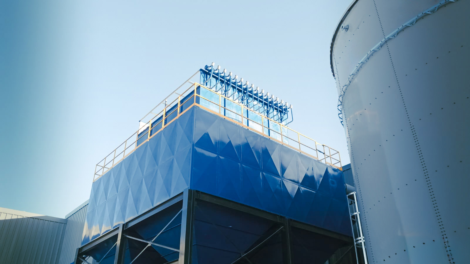 Colector de polvo tipo baghouse azul con pasarela y cabezal de limpieza por pulso junto a silo