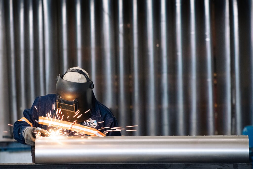 Operador con careta realizando soldadura y corte/esmerilado en pieza metálica con chispas en taller industrial