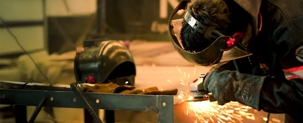 Técnico con careta y guantes realizando esmerilado en metal con chispas en taller de fabricación industrial